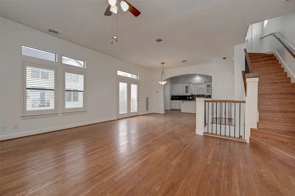 an empty room with wooden floor a chandelier fan and windows