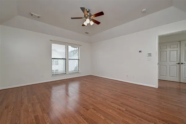 an empty room with wooden floor chandelier fan and windows