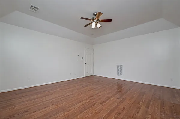 a view of an empty room with wooden floor and a ceiling fan