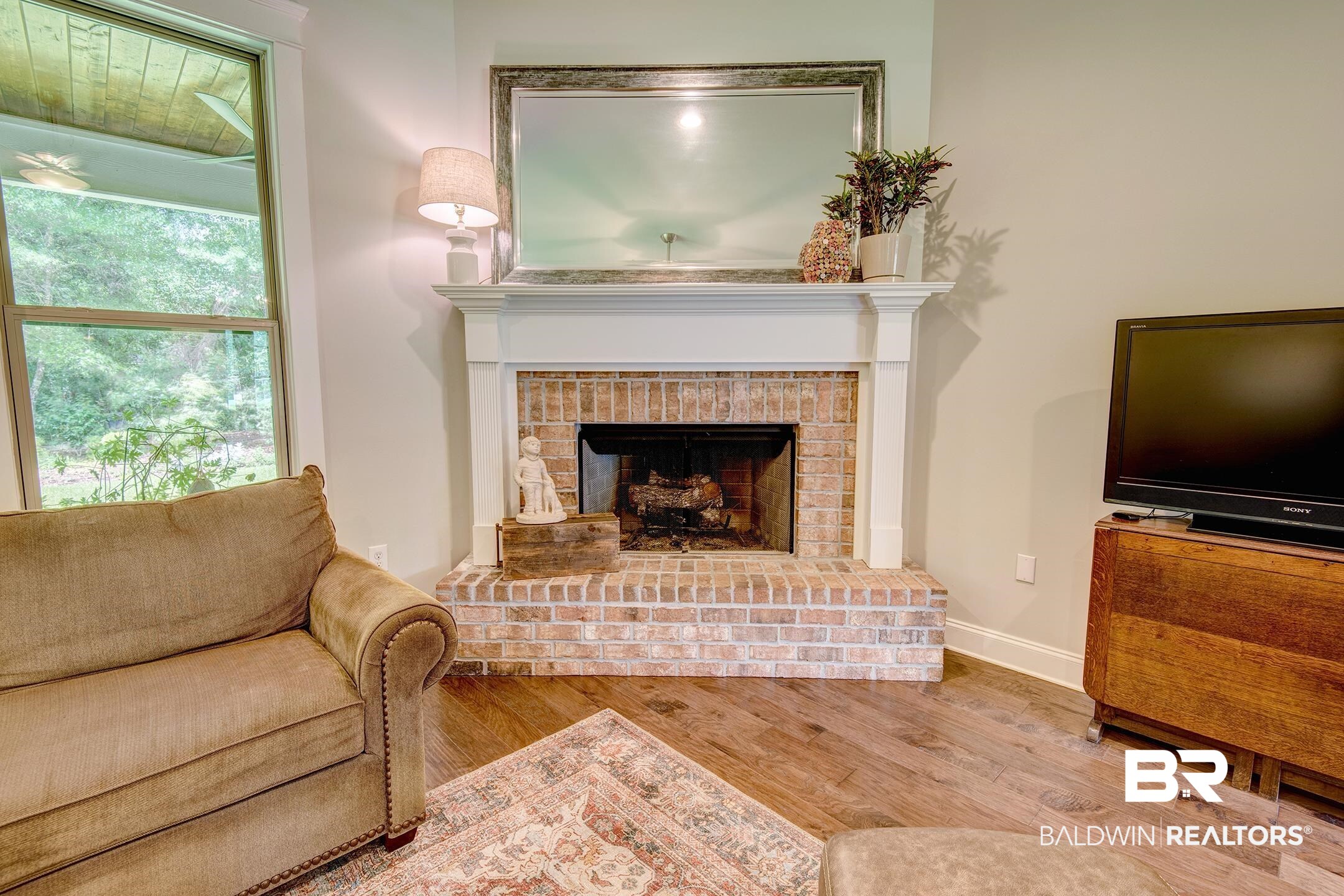18754 Treasure Oaks Road Gulf Shores, AL 36542 - Photo 29 of 53 Brick fireplace with a white mantel and hearth, wood-finish flooring, and a large window providing natural light