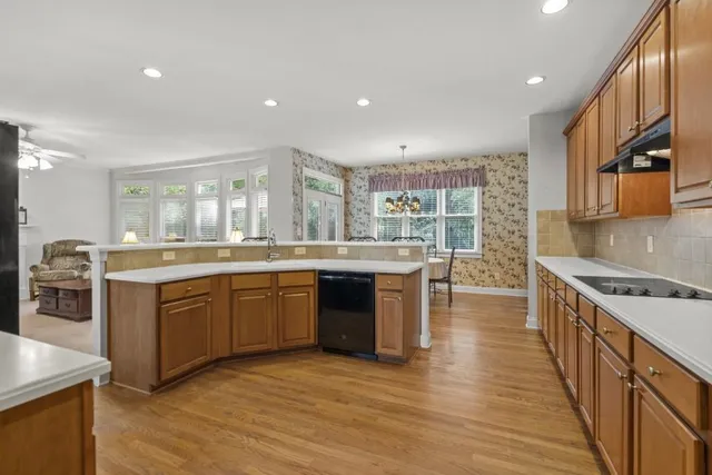 a kitchen with stainless steel appliances granite countertop a refrigerator a sink dishwasher a stove and a dining table with wooden floor