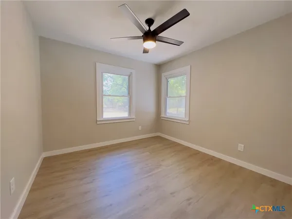 an empty room with wooden floor ceiling fan and windows