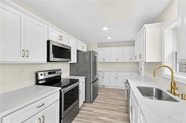 a kitchen with stainless steel appliances granite countertop a sink a stove top oven a refrigerator with white cabinets and wooden floor