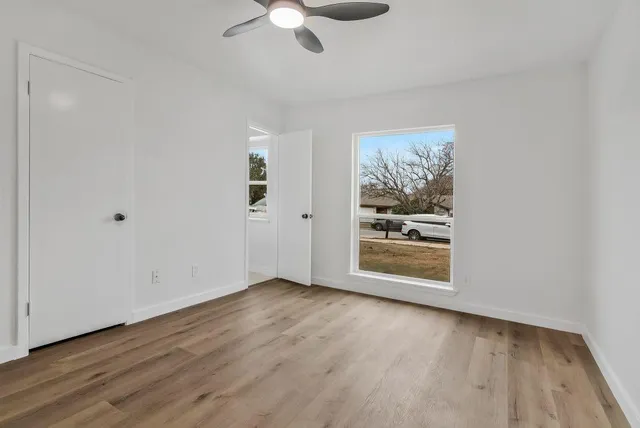 an empty room with wooden floor chandelier fan and windows