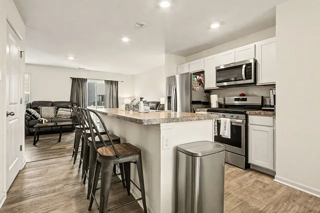 a kitchen with stainless steel appliances granite countertop a stove top oven a sink a dining table and chairs with wooden floor