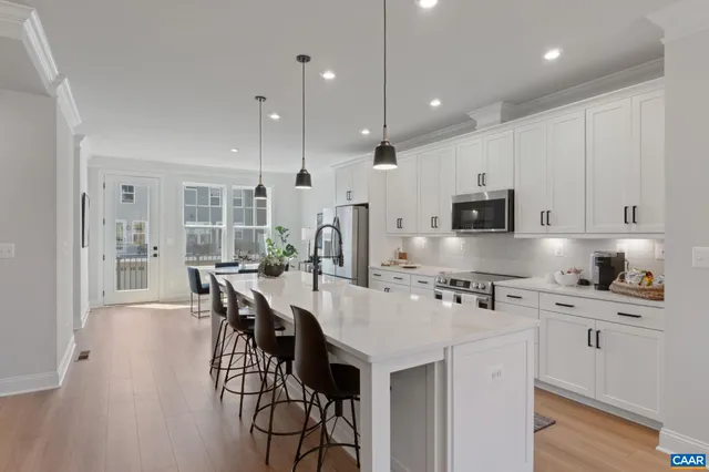 a kitchen with stainless steel appliances kitchen island granite countertop a stove a sink a refrigerator and white cabinets with wooden floor