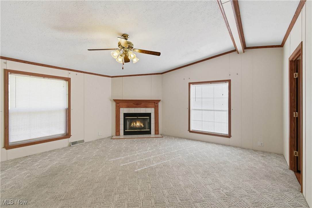 60602 Shaw Road Cambridge, OH 43725 - Photo 7 of 41 Unfurnished living room with a tile fireplace, ceiling fan, ornamental molding, light carpet, and a textured ceiling