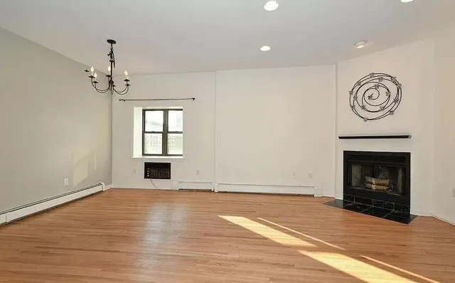 a view of an empty room with wooden floor fireplace and a window