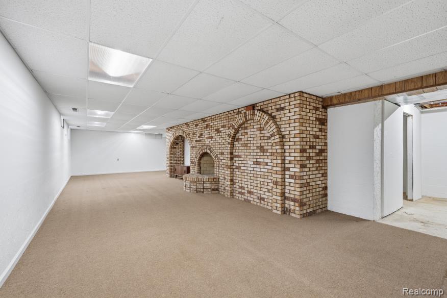 7020 Rattalee Lake Road Clarkston, MI 48348 - Photo 41 of 47 Spacious room featuring a prominent brick-finish wall with arched alcoves, light-colored carpeting, a suspended ceiling with integrated fluorescent lighting, and painted white walls