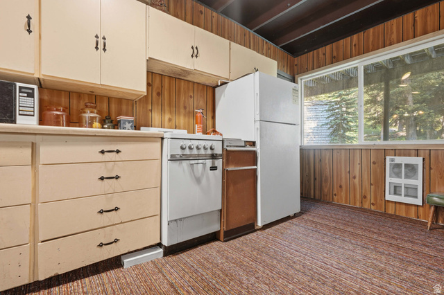 8505 South Snake Crk Road Salt Lake City, UT 84121 - Photo 22 of 67 Kitchen space featuring wood paneling, a large window, light-toned cabinetry with dark hardware, a white freestanding range, and a white refrigerator