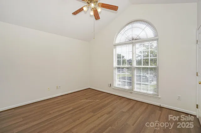 an empty room with wooden floor fan and windows