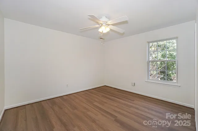 an empty room with wooden floor fan and windows