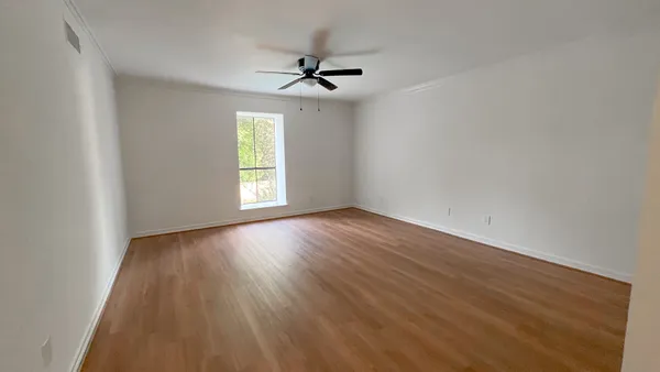 an empty room with wooden floor chandelier fan and windows