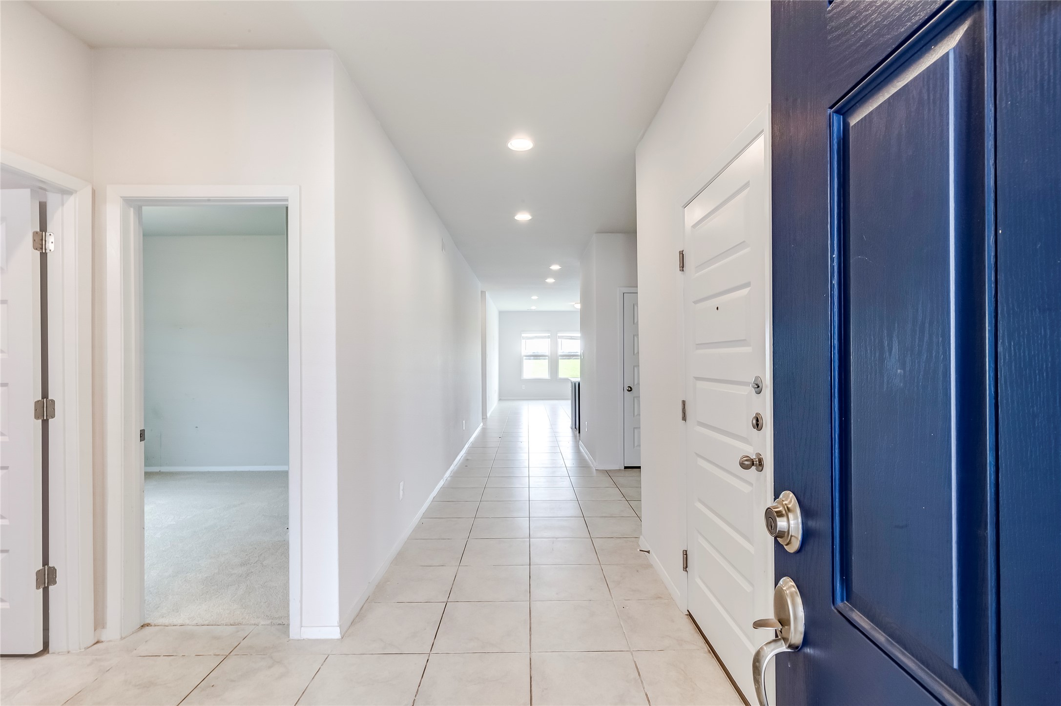 2721 Winding Creek Road Kyle, TX 78640 - Photo 3 of 27 Entryway featuring a vibrant blue front door, tile flooring, recessed lighting, and a long hallway with light-colored walls