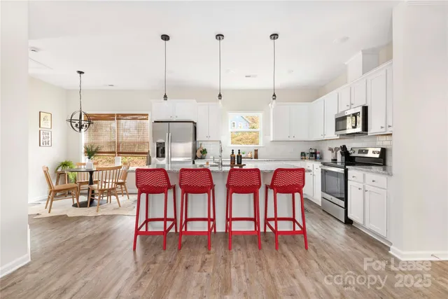 a open kitchen with stainless steel appliances granite countertop a stove a refrigerator a kitchen island with a dining table and chairs with wooden floor
