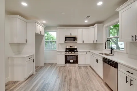 a kitchen with granite countertop a stove top oven a sink dishwasher and a refrigerator with wooden floor