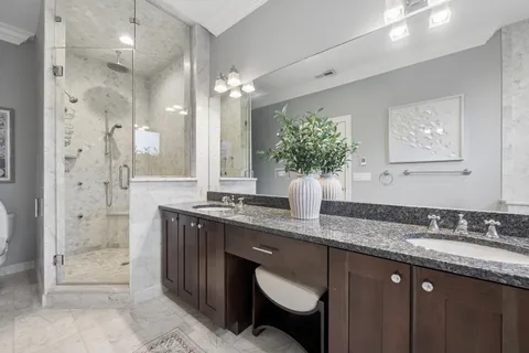 a bathroom with a granite countertop double vanity sink mirror and shower