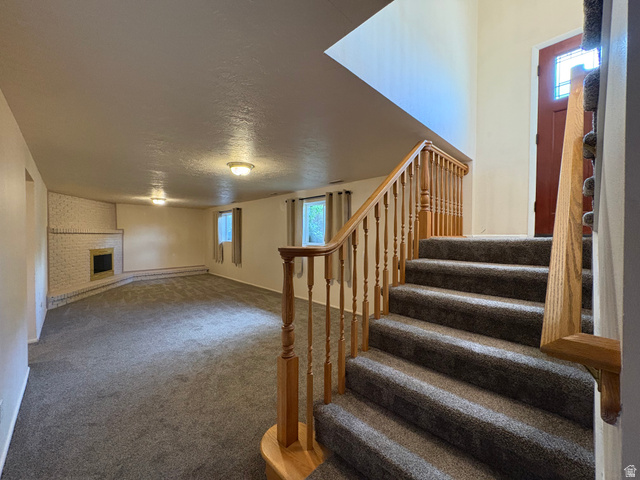 595 Meadowlark Road Orem, UT 84097 - Photo 49 of 87 Carpeted staircase with natural wood railing leading to a spacious lower level featuring a white brick fireplace with a raised hearth, multiple windows, and overhead lighting