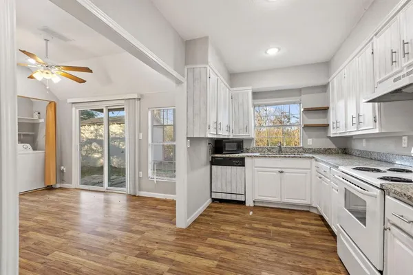 a kitchen with stainless steel appliances granite countertop a stove top oven a sink dishwasher a refrigerator and white cabinets with wooden floor
