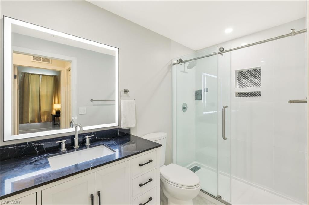 5717 Lago Villaggio Way Naples, FL 34104 - Photo 26 of 35 a bathroom with a granite countertop sink toilet mirror and shower