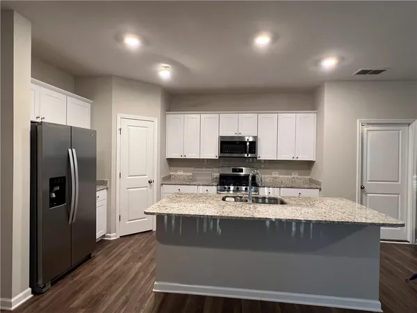 a kitchen with stainless steel appliances kitchen island granite countertop a refrigerator a stove and a sink with wooden floor