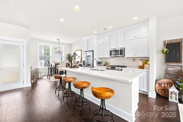 a kitchen with stainless steel appliances granite countertop a stove a refrigerator a kitchen island a dining table and chairs with wooden floor