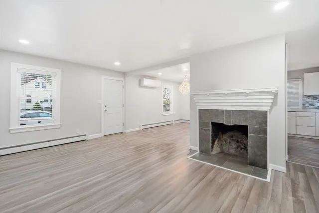 a view of an empty room with wooden floor fireplace and a window