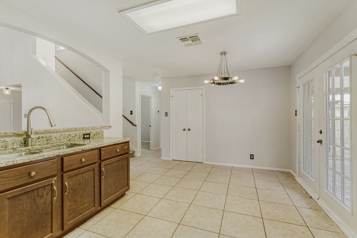 4010 Reeders Drive Austin, TX 78725 - Photo 13 of 26 Kitchen featuring a chandelier, brown cabinetry, light stone counters, light tile patterned floors, and pendant lighting