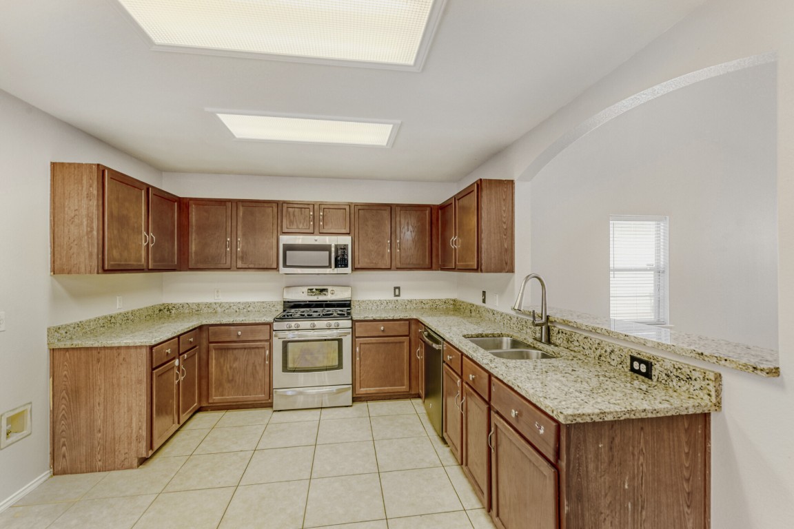 4010 Reeders Drive Austin, TX 78725 - Photo 15 of 26 Kitchen featuring light stone countertops, appliances with stainless steel finishes, brown cabinets, and light tile patterned flooring
