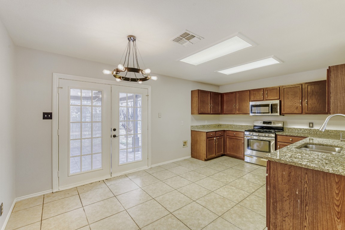 4010 Reeders Drive Austin, TX 78725 - Photo 16 of 26 Kitchen featuring appliances with stainless steel finishes, light stone counters, hanging light fixtures, a chandelier, and light tile patterned floors