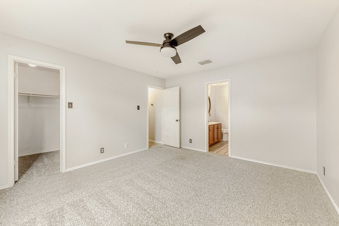 4010 Reeders Drive Austin, TX 78725 - Photo 19 of 26 Unfurnished bedroom featuring a walk in closet, light colored carpet, ceiling fan, and ensuite bathroom