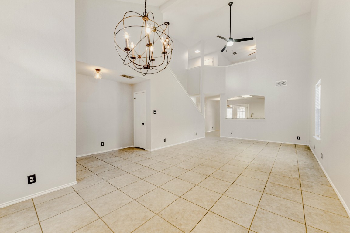 4010 Reeders Drive Austin, TX 78725 - Photo 7 of 26 Unfurnished living room featuring a towering ceiling, a ceiling fan, light tile patterned floors, and a chandelier