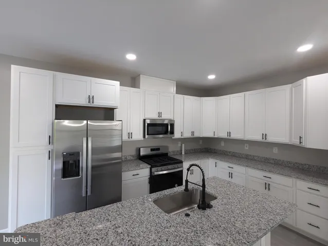 a kitchen with granite countertop a refrigerator sink and white cabinets
