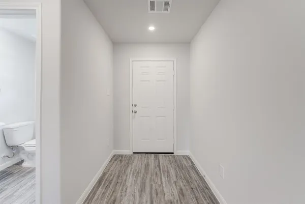 a view of a hallway with wooden floor and a toilet