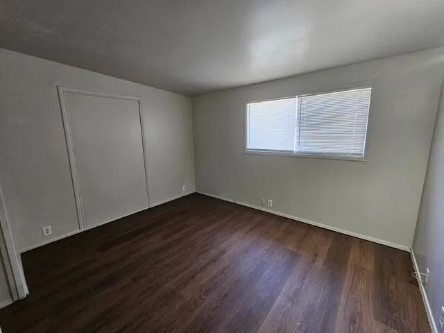 a view of an empty room with wooden floor and a window