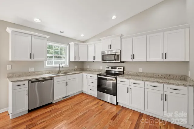 a kitchen with stainless steel appliances granite countertop a stove top oven a sink dishwasher and white cabinets with wooden floor