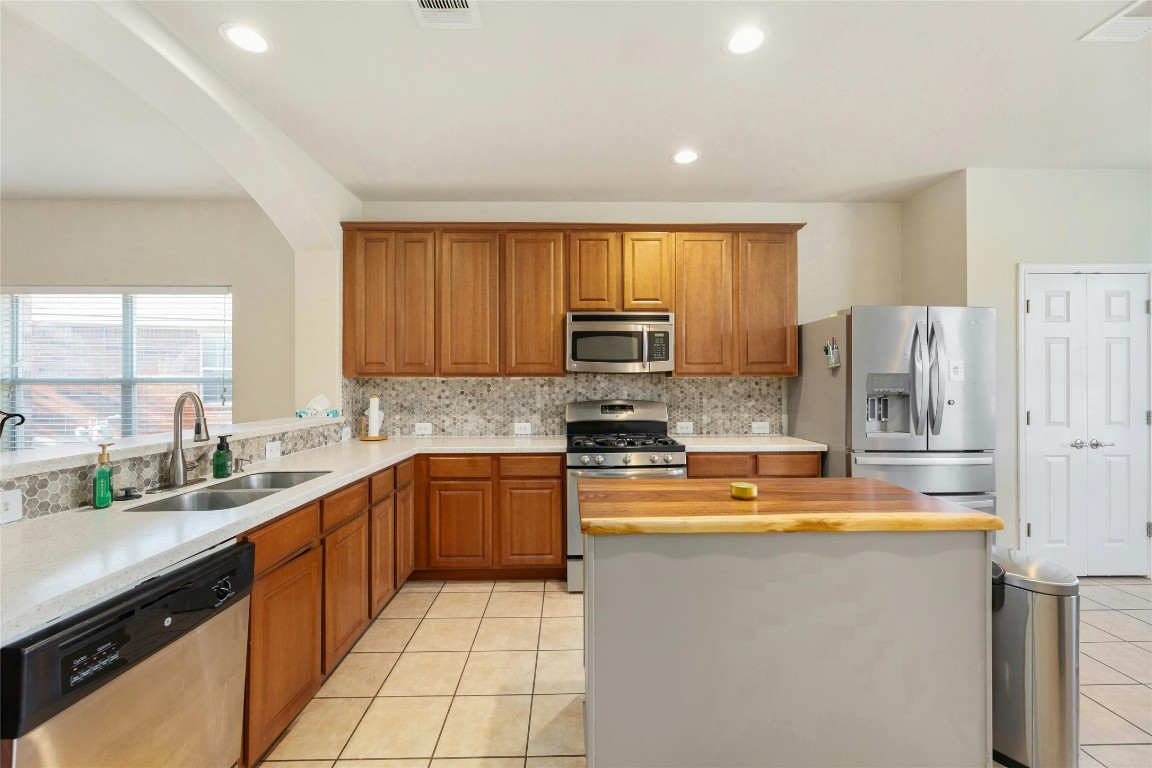 18401 Masi Loop Pflugerville, TX 78660 - Photo 7 of 29 Kitchen with stainless steel appliances, light tile patterned floors, decorative backsplash, brown cabinets, and recessed lighting