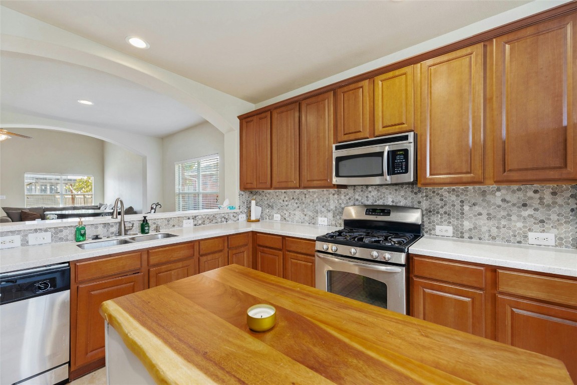 18401 Masi Loop Pflugerville, TX 78660 - Photo 9 of 29 Kitchen featuring appliances with stainless steel finishes, decorative backsplash, arched walkways, brown cabinets, and recessed lighting
