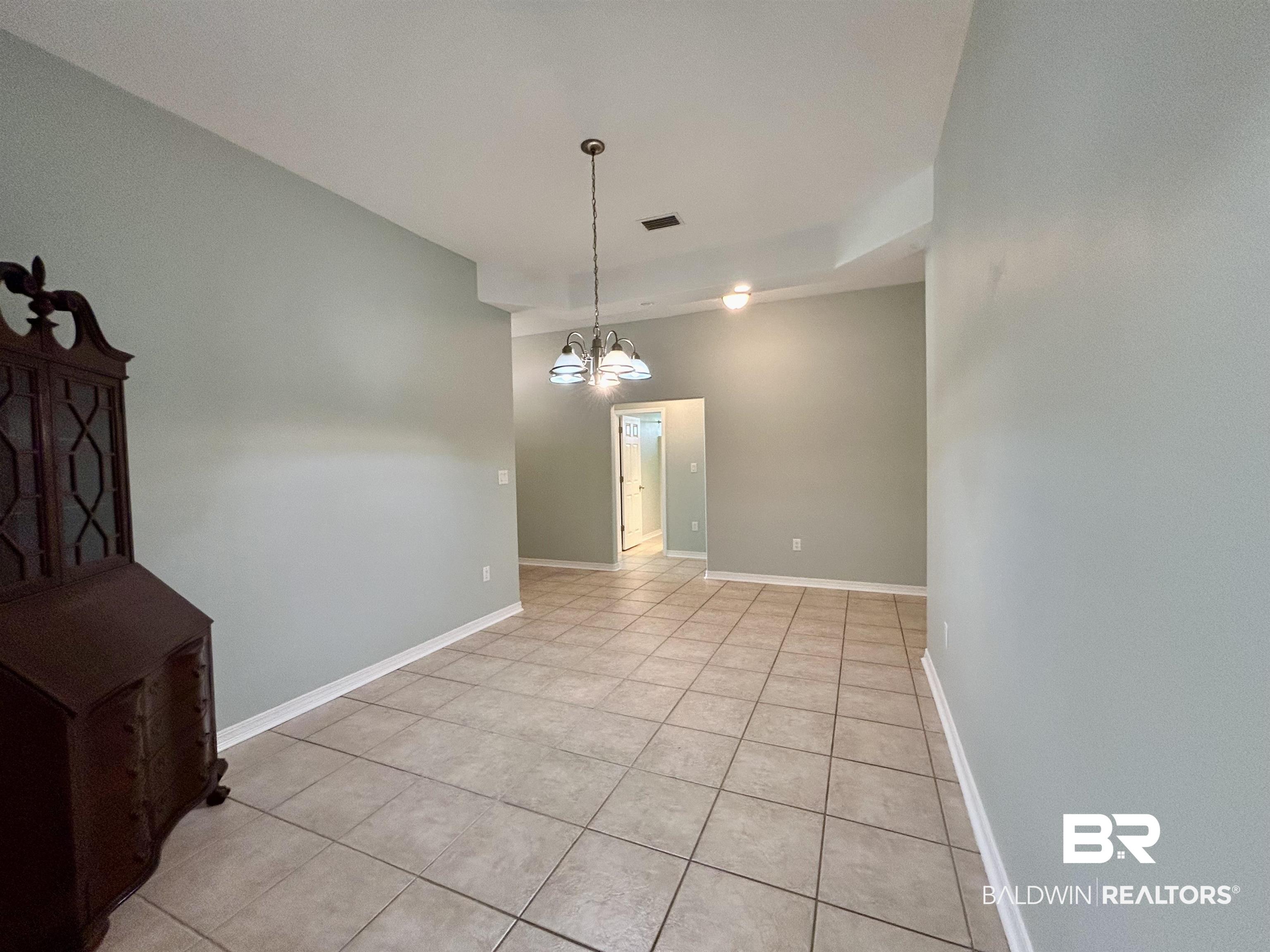 7198 Raintree Lane Gulf Shores, AL 36542 - Photo 10 of 33 Spacious interior room featuring light-colored tile flooring, neutral wall tones, white baseboards, and a tray ceiling