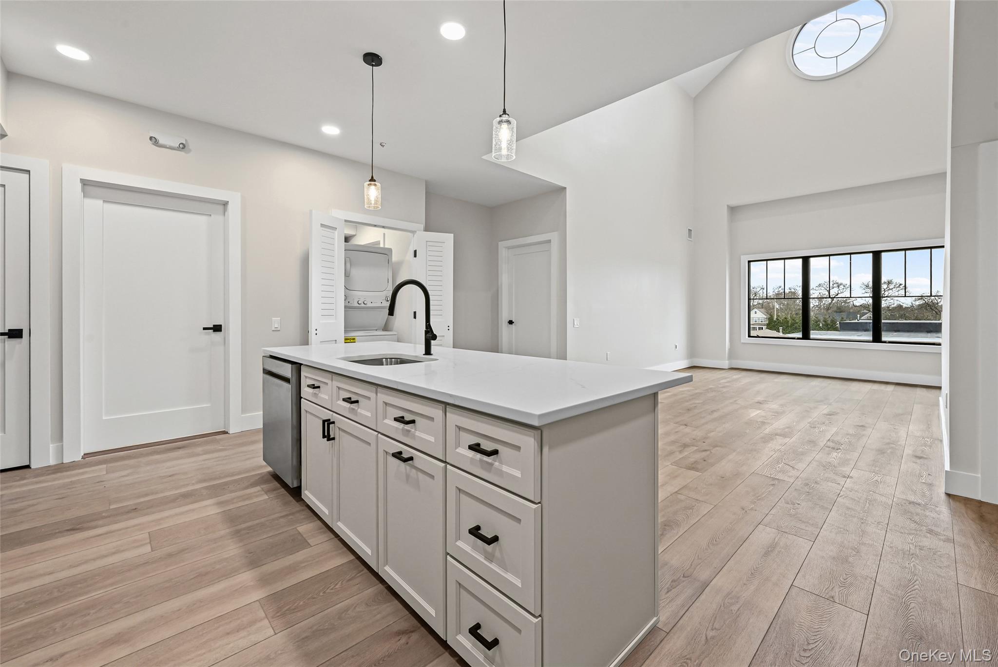 80 Division Street, Unit 3A Patchogue, NY 11772 - Photo 5 of 18 Kitchen featuring white cabinets, hanging light fixtures, light wood-style flooring, a center island with sink, and vaulted ceiling