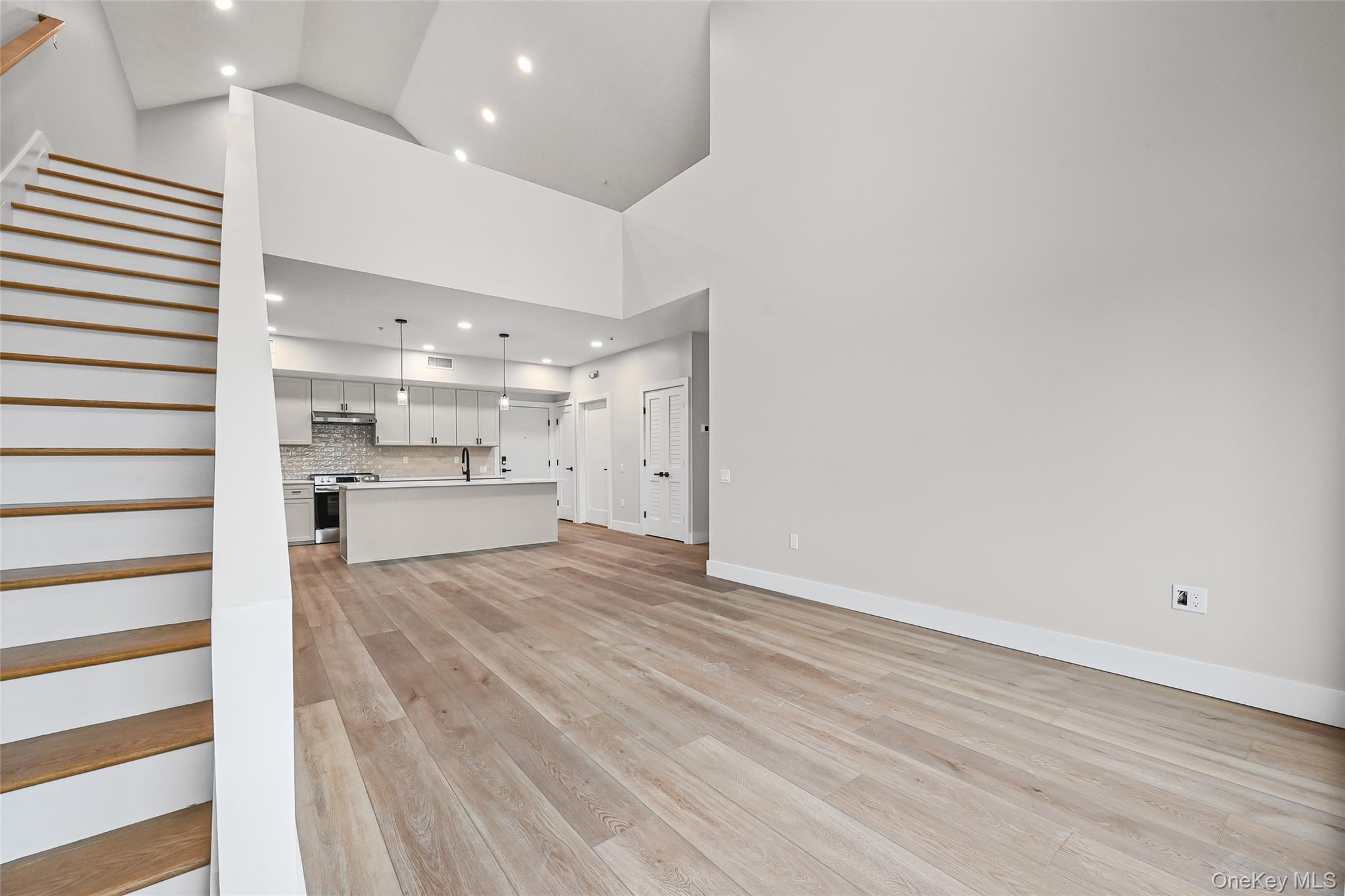 80 Division Street, Unit 3A Patchogue, NY 11772 - Photo 8 of 18 Unfurnished living room featuring light wood-type flooring, recessed lighting, high vaulted ceiling, and stairway