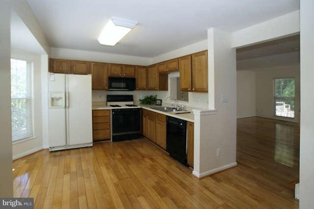 12846 Silvia Loop Woodbridge, VA 22192 - Photo 16 of 30 a kitchen with stainless steel appliances a stove a refrigerator a sink a microwave oven and a dining table with wooden floor
