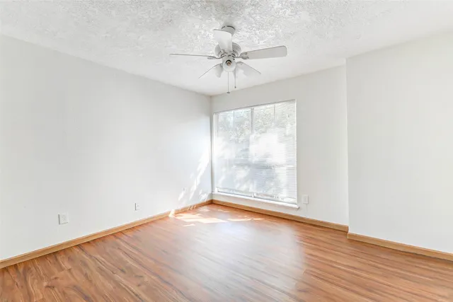 an empty room with wooden floor fan and windows