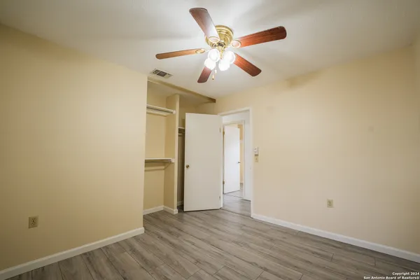 an empty room with wooden floor fan and windows