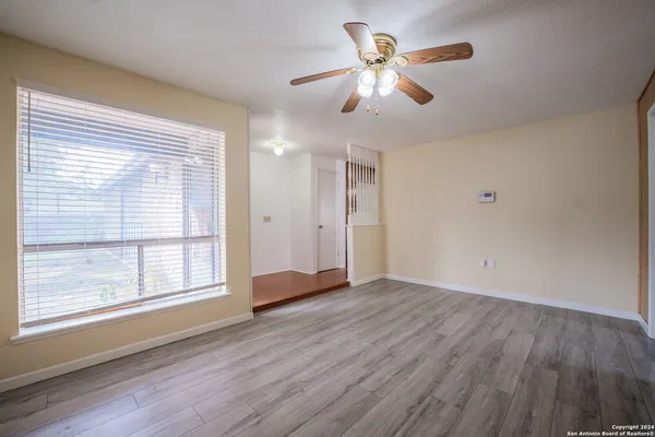 an empty room with wooden floor chandelier fan and windows