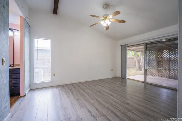 an empty room with wooden floor chandelier fan and windows