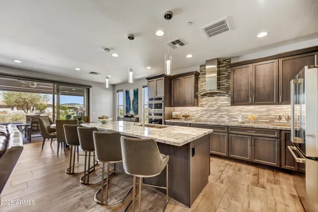 a kitchen with stainless steel appliances granite countertop a stove top oven a sink dishwasher a dining table and chairs with wooden floor