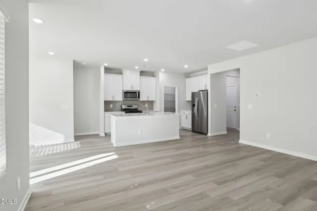 a large kitchen with stainless steel appliances a refrigerator a stove top oven a sink a window and white cabinets