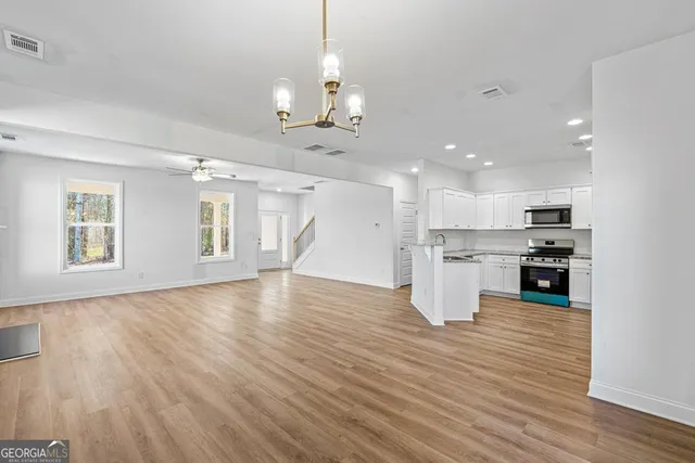 a view of an empty room and kitchen with wooden floor