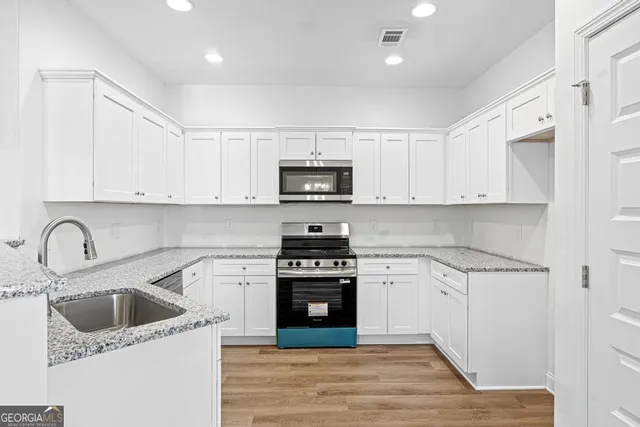 a kitchen with white cabinets a sink and a stove with wooden floor